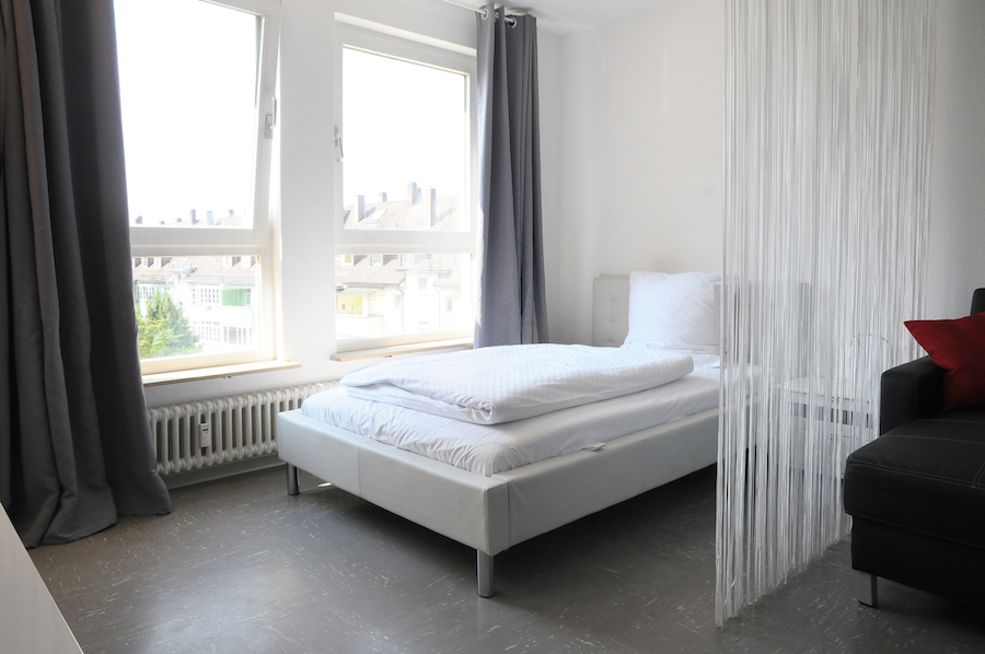 Schlafbereich im Classic Apartment Karlsruhe mit grauen Vorhängen und Raumtrenner
